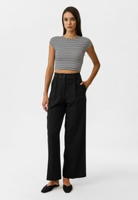 Zwarte wijde broek met plooien aan de voorkant, gecombineerd met een cropped zwart-wit gestreept topje. Minimalistisch ontwerp met een knoopsluiting.