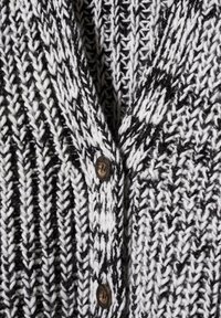 Strickjacke mit einem schwarz-weißen Streifenmuster, V-Ausschnitt und zwei Holzknöpfen. Strukturierte, dicke Wolle verleiht Tiefe.