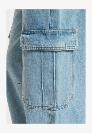 Heledsinine denimi jakk, mille taskul on nähtav õmblus, tekstuuriga kangas ja kerge läige, flapi sulgemisega disain.