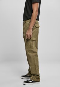 Pantalons cargo en coton vert olive avec une coupe droite, dotés de poches latérales et d'une texture lisse et robuste. Portés avec des baskets noires.