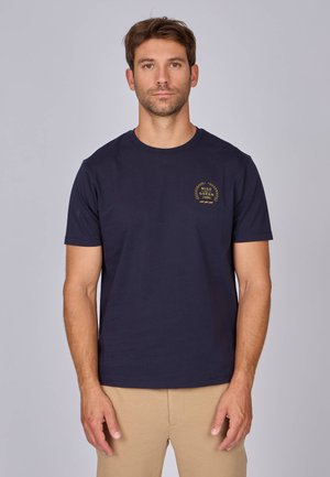 T-shirt à manches courtes bleu marine en coton, avec un logo doré brodé sur la poitrine gauche et un col rond.