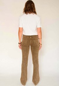 Jean flare marron et t-shirt blanc. Le jean présente une finition texturée avec deux poches arrière et des détails de coutures le long des jambes.