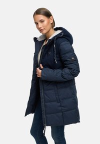 Giacca imbottita blu navy con cappuccio, foderata in pile testurizzato, chiusura frontale con zip e tasche laterali. Presenta un design trapuntato e dettagli con cordino.
