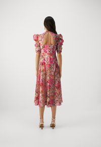 Vestido midi floral en tonos rosas con mangas abullonadas y espalda descubierta. Tejido transparente con texturas delicadas. Combinado con tacones blancos de tiras.
