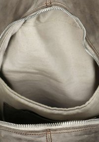 Interior de una bolsa de tela gris con un forro beige. Presenta un zipper plateado en la apertura y costuras marrones en el borde exterior.