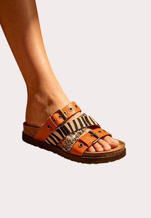 Pied portant une sandale à bout ouvert en cuir marron avec deux brides imprimé animal, boucles réglables et semelle en liège.