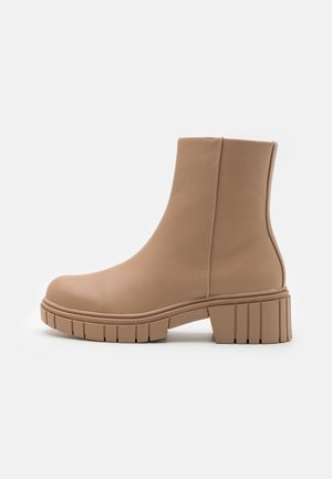 Botas de tobillo beige hechas de cuero suave, con punta redondeada, tacón de bloque de altura media y suela segmentada texturizada.