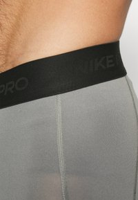 Sive kratke sportske hlače s crnim pojasom na kojem je natpis "NIKE PRO". Tkanina izgleda glatko, s vidljivim šavovima.