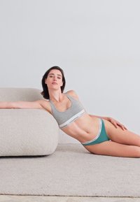 Grijze sportbeha met een witte band, gecombineerd met teal slips met witte accenten, beide gemaakt van soepel materiaal, tegen een neutrale achtergrond.