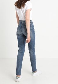 Modré džíny s vysokým pasem, zúženým střihem, vybledlým omráčením a třepeným lemem. Kombinované s bílou košilí s krátkým rukávem a bílými teniskami.