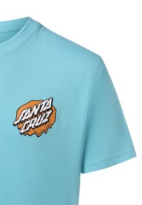 Camiseta de manga corta azul claro con cuello redondo. Presenta un logotipo gráfico en negro y naranja en el pecho izquierdo que dice "Santa Cruz Skateboards".