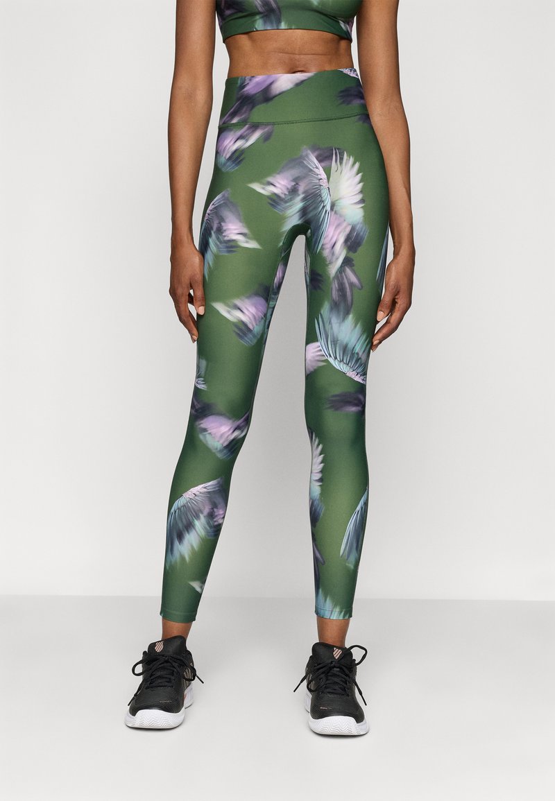 Green leggings featuring a fluid, abstract pattern of purple and teal feathers. Paired with a matching crop top and black athletic shoes.