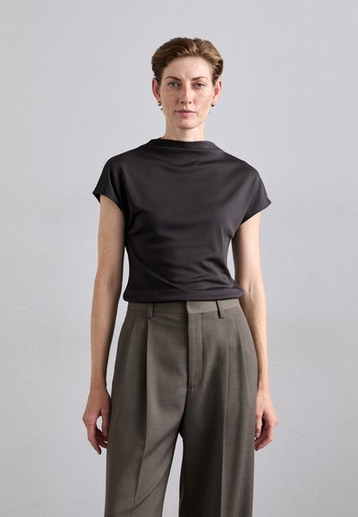 Dark gray short-sleeve top with a high neckline, complemented by tailored, light gray pleated trousers, featuring a smooth fabric texture.