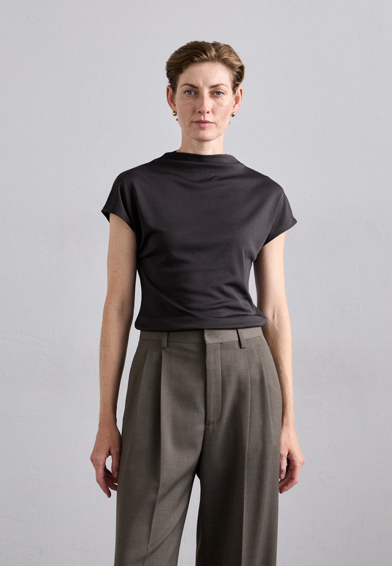 Dark gray short-sleeve top with a high neckline, complemented by tailored, light gray pleated trousers, featuring a smooth fabric texture.