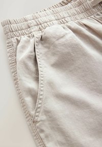 Licht beige shorts van zacht materiaal, met een elastische tailleband, zijzakken en een textuursteek langs de naden.