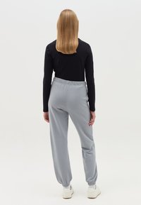 Helle graue Jogginghose mit elastischem Bund und Bündchen, kombiniert mit einem figurbetonten schwarzen Langarmoberteil. Heller Stoff mit lockerer Passform.