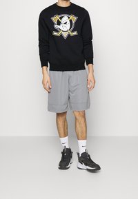 Svart sweatshirt med tryckt logotyp, gråa shorts och svarta sneakers med vita detaljer. Bomullsmaterial, avslappnad passform och strumpor i ankellängd.