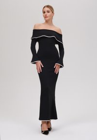 Svart off-shoulder klänning med vit kant, figurnära långärmar och utsvängd nederdel. Slät textur och kroppsnära silhuett.
