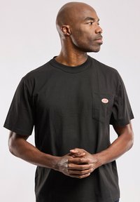 Schwarz Baumwoll-T-Shirt mit kurzen Ärmeln, ausgestattet mit einer Brusttasche auf der linken Seite und einem ovalen Logopatch. Schlichtes, klassisches Design und lockere Passform.