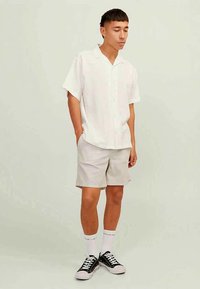 Hvid kortærmet skjorte med knaplukning parret med lyse beige shorts. Modellen bærer sorte sneakers og hvide sokker med mærker. En simpel, afslappet påklædning.