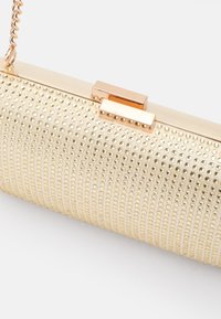 Clutch dorato con superficie texture decorata con piccoli chiodini, dotata di una chiusura rettangolare e una tracolla rimovibile.