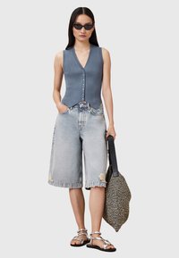 Hellblau gerippter ärmelloser Oberteil mit V-Ausschnitt und Knopfdetails, kombiniert mit ausgewaschenen, zerfetzten Bermudashorts aus Denim und Riemchensandalen.