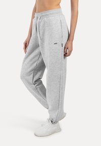 Grijze sweatpants van zacht materiaal, met een taps toelopende boord, zijzakken en een trekkoord in de tailleband. Gecombineerd met witte sneakers.
