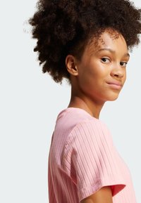 Rózsaszín, bordázott, rövid ujjú felső, kerek nyakkivágással, textúrált csíkokkal és laza szabással. Simább anyag, amely enyhe fényt ad.