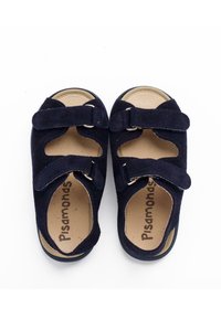 Navy blue suede sandals with two adjustable straps, cutout design, tan insole with branding. Flat sole and rounded toe shape.