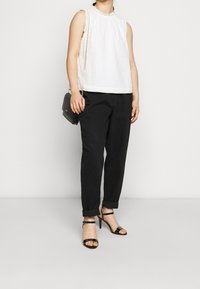 Vit utanärmad topp med texturerat tyg och rund halsringning, matchad med svarta uppvikta byxor och svarta klacksandaler. Liten svart handväska.