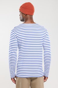 Gestreiftes Langarmshirt in Weiß und Blau mit Rundhalsausschnitt; Modell trägt hellbraune Hose und eine strukturierte orangefarbene Mütze.
