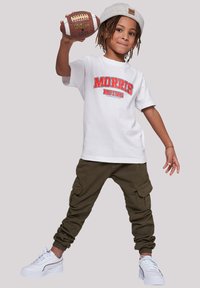 White short-sleeve t-shirt with "MORRIS MOTORS" print, olive cargo pants, and white sneakers. Model holds a brown football.