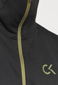 Felpa nera con zip e collo alto, caratterizzata da una cerniera di colore verde oliva a contrasto e dal logo CK in un colore abbinato sul davanti.