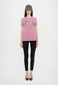 Rosa t-skjorte med kort erme og blomsterdesign samt teksten "COUTURE", kombinert med svarte skinny jeans og en mørk grå caps. Svarte spisse hæler.