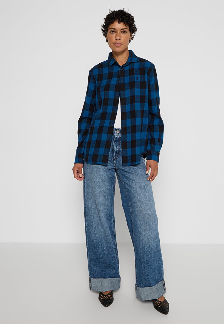 Camicia a quadri nera e blu con design a bottoni, maniche lunghe e colletto, abbinata a jeans in denim a gamba larga.