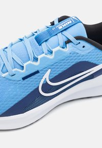 Light blue athletic shoe with mesh upper, dark blue accents, white swoosh logo, textured sole, and blue laces. Features a padded collar.