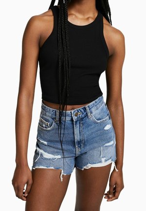 Crop top noir à côtes associé à un short en denim bleu déchiré. Le short a des bords effilochés et des déchirures bien visibles.