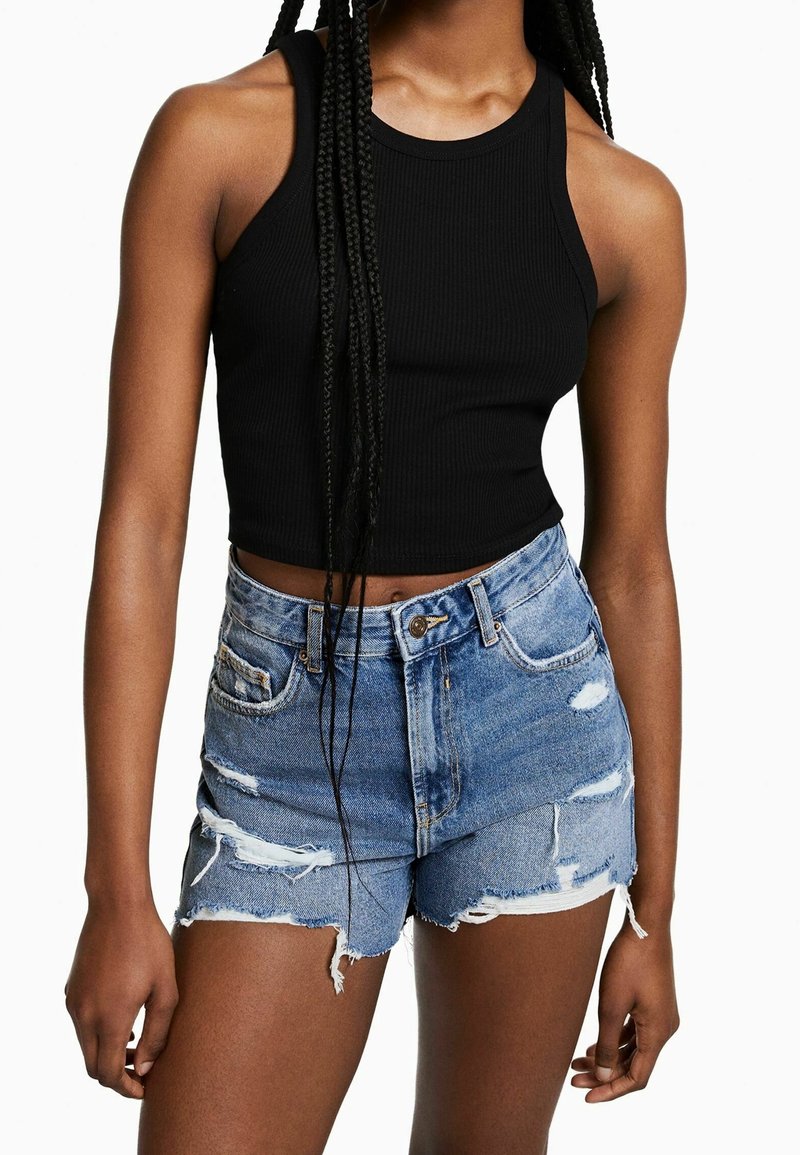 Svart ribbad crop top i kombination med blå slitna denimshorts. Shortsen har fransade kanter och framträdande hål.