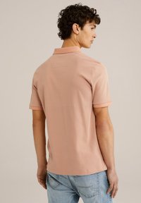 Polo shirt cu mânecă scurtă în roz deschis, cu un model geometric subtil, guler și o croială lejeră. Purtați-l cu blugi albaștri, arătând din spate.