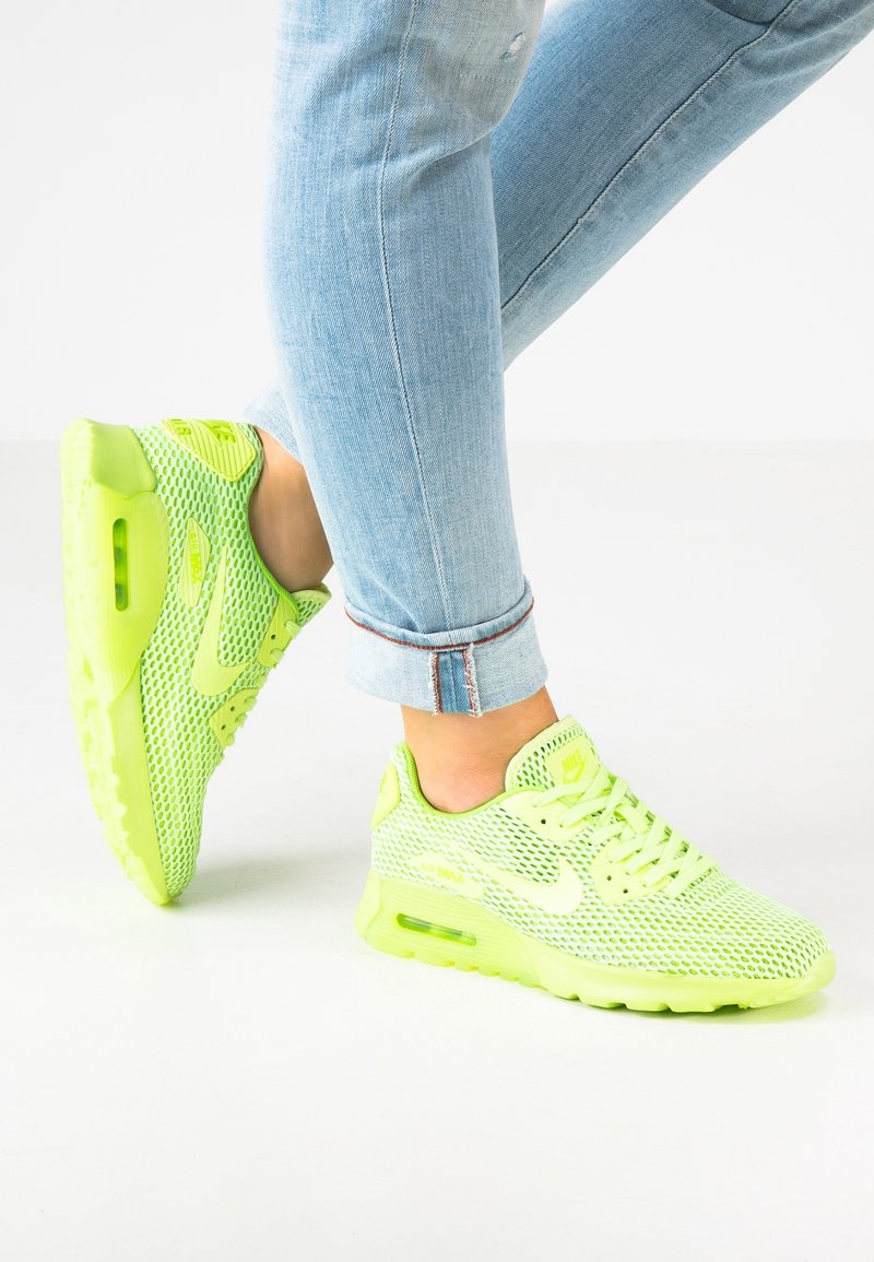 Person wearing light blue rolled-up jeans and bright neon green Nike Air Max sneakers on a white floor.