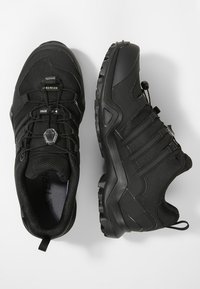 Czarne sportowe buty z materiałową cholewką, gumową podeszwą, bezsznurowym designem z zapięciem na toggle oraz wzmocnionym czubkiem dla większej trwałości.