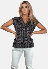 Czarny top z dekoltem w kształcie litery V, krótkimi rękawami i białym wzorem w kropki. Zestawiony z białymi spodniami, tworzy dopasowaną sylwetkę.