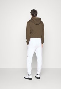 Afskåret brun hættetrøje med hætte, parret med hvide sweatpants med sidelommer og et rødt logo, båret med hvide chunky sneakers.