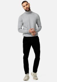 Jasnoszary sweter z golfem, dopasowane czarne spodnie z korduroju i kremowe trampki. Gładka faktura, dopasowany krój i monochromatyczna kolorystyka.