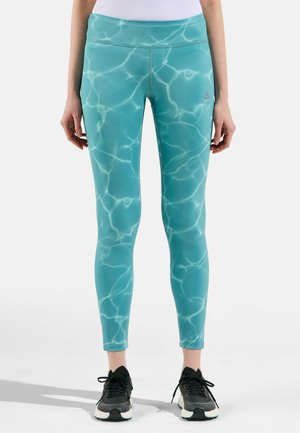 Aqua leggings with a water-like pattern, stretchy material, high waistband, and logo detail on the left side, paired with black athletic shoes.