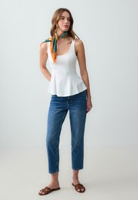 Witte peplum tanktop, donkerblauwe cropped jeans, bruine gevlochten slidesandalen en een meerkleurige zijden sjaal geknoopt om de hals.