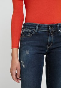 Mörkblåjeans med en lätt tvätt och slitna partier. Har en klassisk femfickdesign och en midjehöjd som är genomsnittlig.