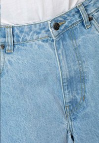 Jeans de denim azul claro con cintura alta, bolsillos frontales, costuras doradas en contraste y cierre de botón de metal negro.