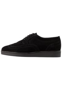 Scarpe brogue nere in suede con perforazioni decorative, bordi lisci e suola piatta in gomma. Lacci e cuciture in un design tonale.