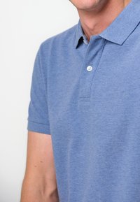 Blå polo tröja i texturerad tyg, med korta ärmar, krage och två knappslå som visar ett subtilt melerat mönster.